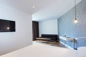 Ein modernes Hotelzimmer mit Fernseher an der Wand, Sofa und Schreibtisch.