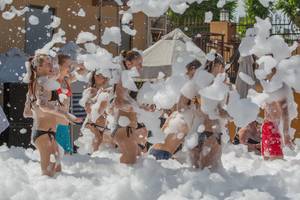 Mehrere Leute auf einem Seifenblasenfest in Badekleidung, umgeben von großen Seifenblasen.