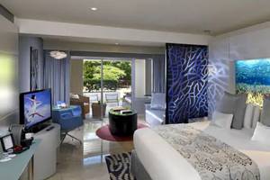 Innenansicht eines Zimmers im Paradisus Playa del Carmen Hotel mit großem Bett, Fernseher, Möbeln und Aquarium-Wandbild.