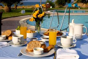 Frühstückstisch mit Orangensaft, Brot und Gebäck am Pool im Plaza Beach Hotel.