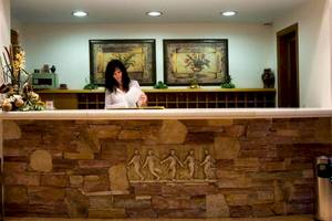 Rezeption des Plaza Beach Hotels mit einer Frau am Schreibtisch und Steinwand im Hintergrund.