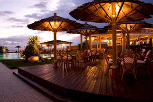 Poolbar des Plaza Beach Hotels bei Sonnenuntergang mit beleuchteten Strohschirmen und Stühlen.