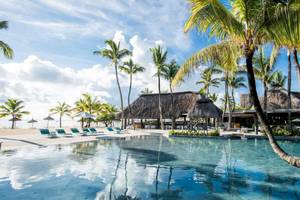 Poolbereich des Long Beach Mauritius Hotels mit Palmen und afrikanischen Hütten.
