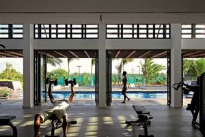 Fitnessstudio im Long Beach Mauritius mit einem Mann, der Hanteln hebt, und einem Pool im Hintergrund.
