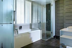 Badezimmer im Long Beach Mauritius Hotel mit Badewanne, Glasdusche und doppelwaschbecken.