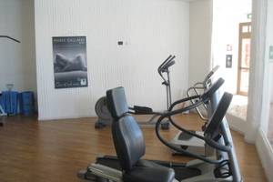 Fitnessbereich im Baia Caddinas Hotel mit mehreren Cardiogeräten und einer Plakatwand.