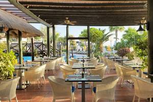 Innenbereich des Restaurants im H10 Timanfaya Palace mit Tischen und Stühlen, umgeben von Pflanzen und Blick auf den Pool.