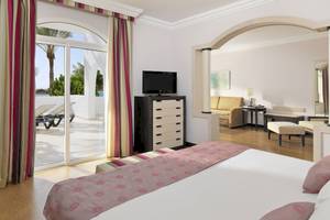 Innenansicht der Suite im H10 Timanfaya Palace Hotel mit Bett, Fernseher, und Blick auf die Terrasse.