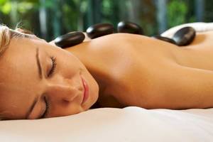 Eine Frau genießt eine Massage im Spa, mit Steinen auf dem Rücken liegend.
