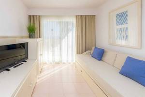 Wohnbereich des Blau Punta Reina Hotels mit Fernseher, Couch, Kissen und Gemälde.