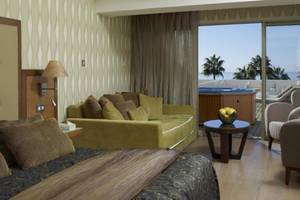 Hotelzimmer im Atlantica Miramare Beach Hotel mit großem Bett, Sofa, Tisch und Whirlpool auf dem Balkon.