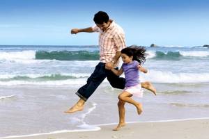 Ein Vater und seine Tochter springen am Strand von Brayka Bay Resort.