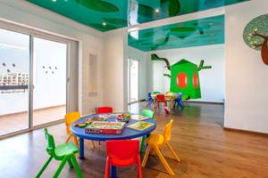 Kinderspielzimmer im Bianca Beach Resort mit bunten Tischen und Stühlen, blauem Tisch, grüner Wandmalerei und bemalter Decke.