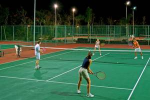 Spieler spielen Tennis auf einem beleuchteten Tennisplatz bei Nacht.