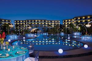 Der beleuchtete Swimmingpool des Secrets Akumal Riviera Maya Hotels bei Nacht mit runden Tischen und Stühlen.
