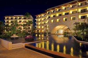 Nachtansicht eines geleuchteten Hotels am Pool mit Lounge-Möbeln, Pflanzen und Bäumen