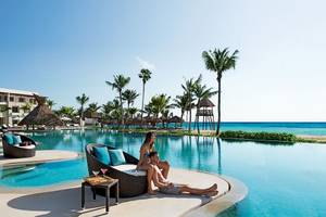 Paar sitzt am Poolrand des Secrets Akumal Riviera Maya Hotels neben einem Lounge-Set.