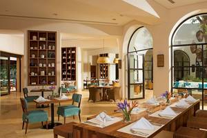 Innenansicht des Restaurants im Secrets Akumal Riviera Maya mit Holztischen, Stühlen und Tischdekoration.