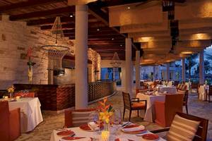 Innenbereich des Secrets Akumal Riviera Maya Hotels mit rustikalem Design, Säulen, Beleuchtung und gedeckten Tischen.