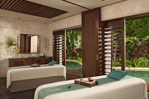 Massageraum im Secrets Akumal Riviera Maya mit Blick auf einen Pool und tropischen Garten.