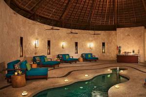 Innenpool des Secrets Akumal Riviera Maya Hotels mit blauen Liegen und Wasserfontäne.