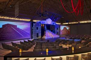 Innenbereich des Theaters im Hotel Secrets Akumal Riviera Maya mit großen Bildschirmen und Sitzplätzen.