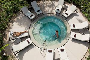 Oberflächenansicht eines Infinity-Pools im Secrets Akumal Riviera Maya Hotel mit mehreren weißen Liegestühlen und grüner Umgebung.
