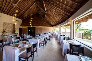 Innenansicht des Restaurants des Reef Coco Beach Hotels mit gedeckten Tischen und hängenden Lampen.