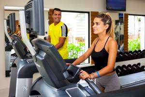 Fitnessstudio im Reef Coco Beach Hotel mit einer Frau auf dem Laufband und einem Mann im Hintergrund.