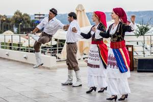 Vier Personen in traditioneller griechischer Kleidung tanzen auf der Terrasse des Kiani Beach Resorts.