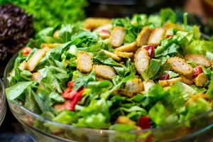 Ein Salat mit grünem Blattwerk, gewürfeltem Huhn und roten Paprikastücken in einer Glasschale.