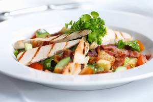 Ein Gericht im weißen Teller mit Salat, gegrilltem Fleisch, Tomaten und Gurken.