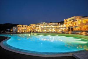 Nachtansicht des Cala Cuncheddi Hotels mit beleuchtetem Swimmingpool und Sonnenliegen.