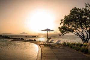 Sonnenuntergang am Cala Cuncheddi Hotel mit Strand, Lounges und einem Schirm
