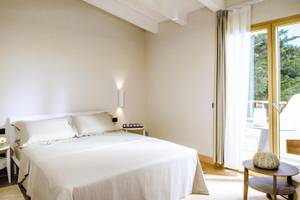 Schlafzimmer im Hotel Cala Cuncheddi mit einem Bett, Kissen, Tisch und Aussicht auf Bäume.