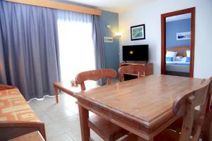 Innenansicht des Zimmers im Bluesea Aloe Corralejo Hotel mit Tisch, Stühlen, Fernseher und Schlafzimmerspiegel.