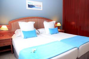 Zwei Betten im Hotelzimmer des BLUESEA Aloe Corralejo mit blauen Kissen und Decken.