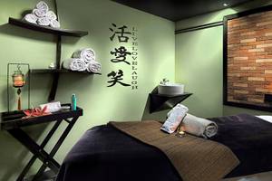 Massageraum im Aparthotel Allegro Isora mit grünen Wänden, Wellness-Produkten und einem japanischen Schriftzug.