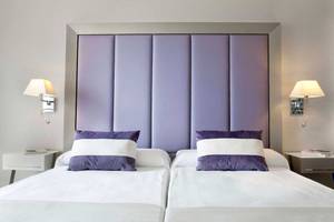 Schlafzimmer mit zwei Betten, lavendelfarbenem Kopfteil und Nachttischen
