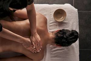 Massagebehandlung im Myconian Avaton Resort mit einer Frau, die einen Rückenmassiert.