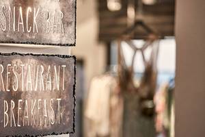 Weiß beleuchtete Schilder an einer Wand im Myconian Avaton Resort, die Snack Bar und Restaurant Breakfast anzeigen.
