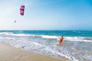 Ein Kitesurfer am Strand mit einer pinken Drachen im Himmel