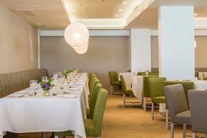 Innenbereich des Restaurants im Nissi Beach Resort mit langen Tischreihen und grünen Stühlen.