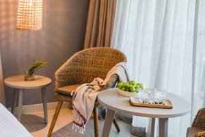 Innenansicht eines Zimmers im Nissi Beach Resort mit Bett, zwei Nachttischen, einem Korbstuhl und einem Tisch mit Früchten.