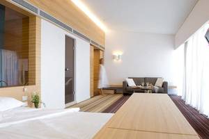Innenansicht eines Hotelzimmers im Doryssa Seaside Resort, mit Bett, Wohnzimmerbereich und Frau im Hintergrund.