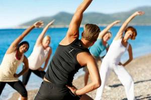 Gruppe von Frauen und Männern, die Yoga am Strand des Doryssa Seaside Resort machen