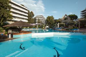 Außenpool des Dionysos Hotels mit Sonnenliegen und Gebäuden im Hintergrund.