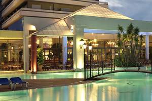 Der Außenpool des Dionysos Hotels bei Nacht mit einer Brücke und Lounge-Stuhl am Pool.