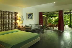 Innenansicht eines Zimmers im Dionysos Hotel mit einem Bett, einer Couch und einem Tisch mit Gartenblick.