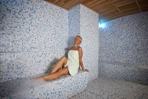 Frau im Saunaraum des Titan Select Hotels mit blauen Fliesen und Holzdecke